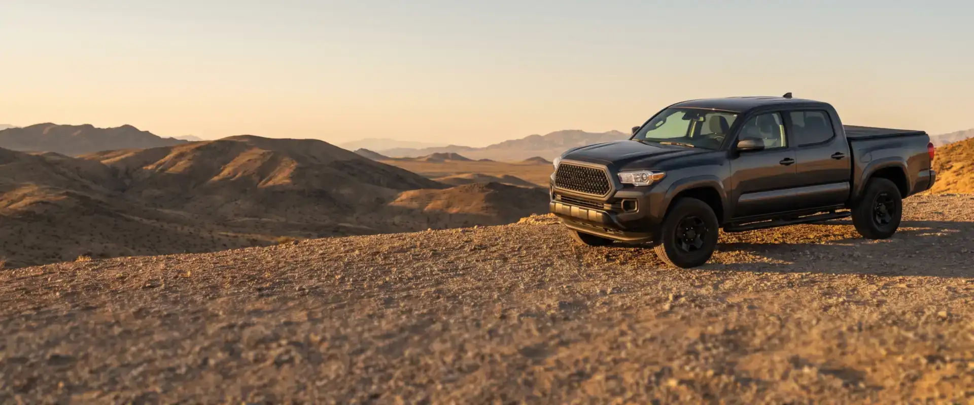 Dark gray crew cab pickup with a hard folding tonneau cover and running boards on a desert overlook
